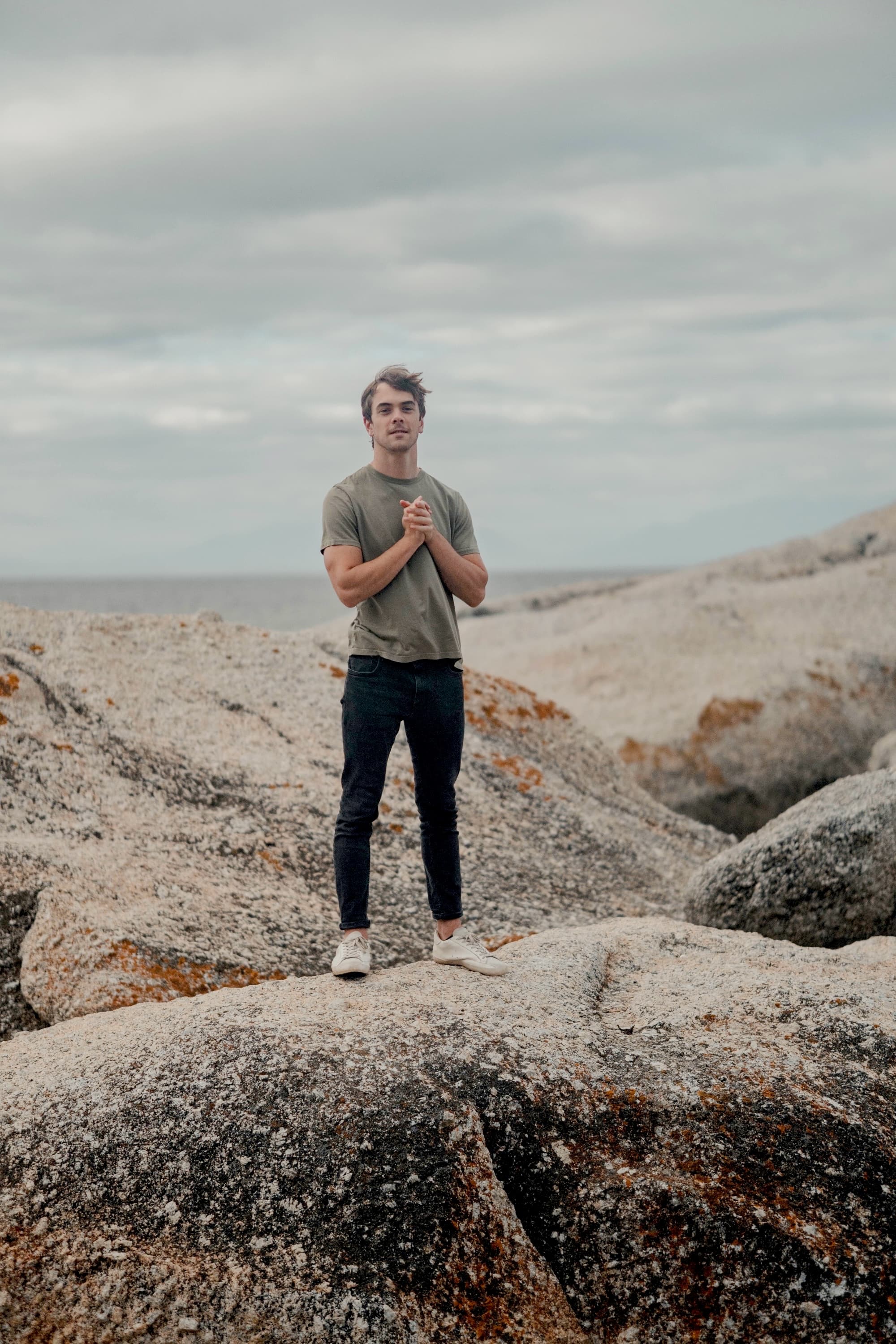 Matt Derman standing among coastal rocks beneath an overcast sky