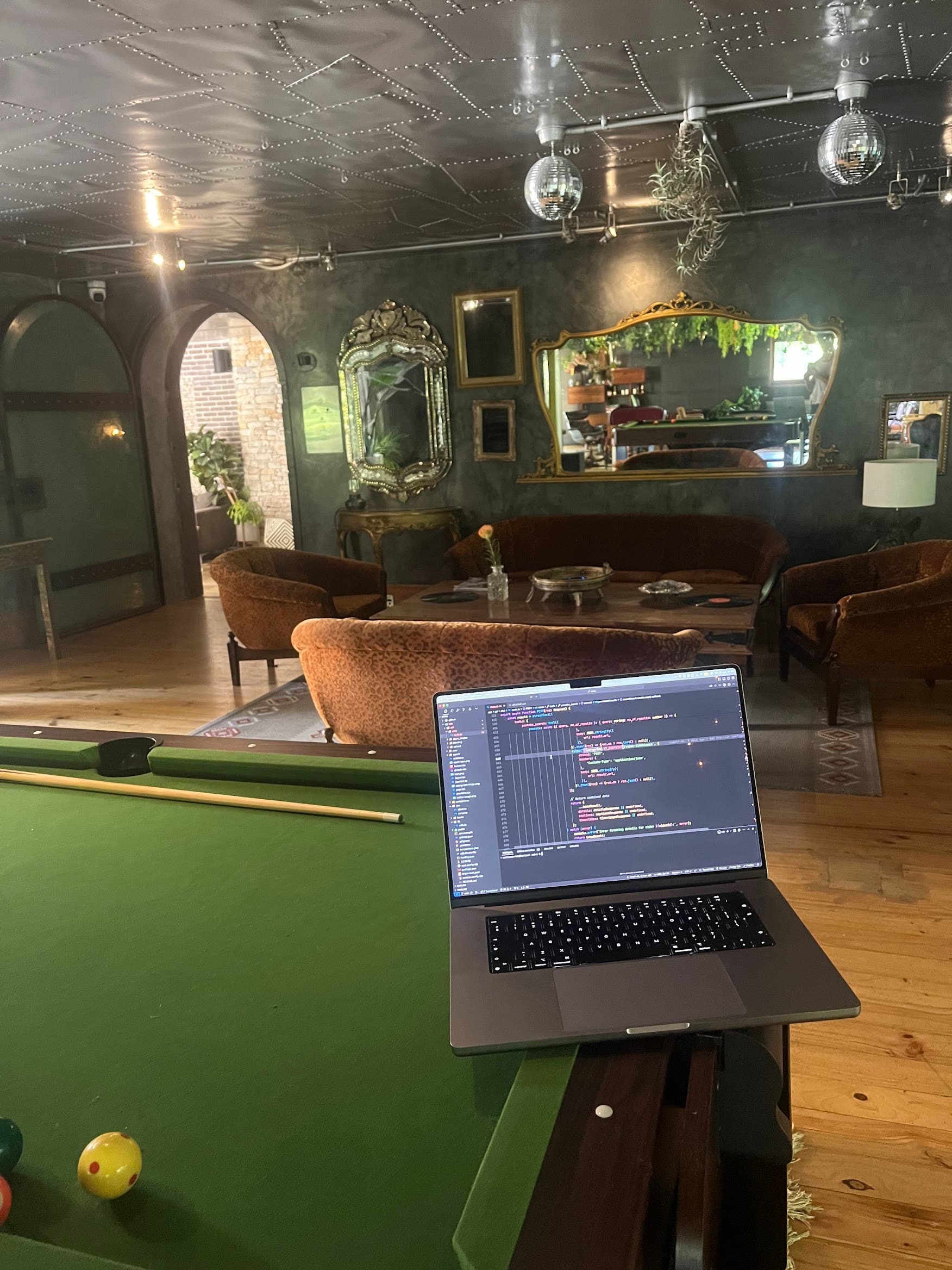 A laptop open beside a pool table in a mirrored studio workspace